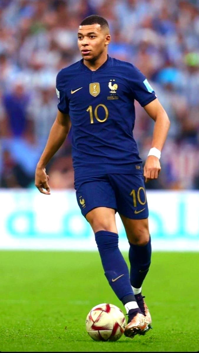 A soccer player in a blue France jersey with number 10 dribbles a ball on the field during a match, as fans and stadium lights blur into the background—a scene you can catch live through Colombia IPTV.