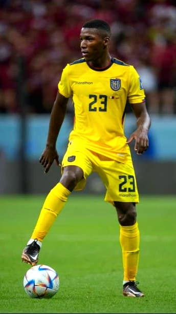 A soccer player in a yellow Ecuador uniform with the number 23 controls a ball on the field during a match, as fans watch the action live through Colombia IPTV.